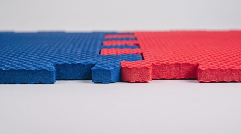 Close-up of interlocking EVA puzzle mats showing dual-color red and blue tiles with high-density foam layers and non-slip texture.