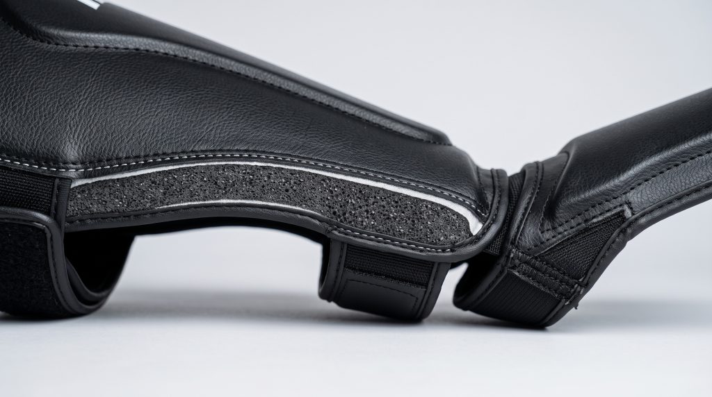 Macro close-up shot of custom martial arts shin guard showing high-density EVA foam inner padding layer and flexible instep joint.